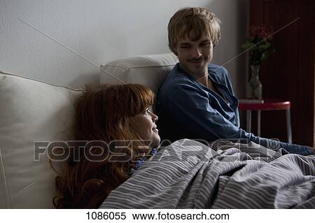 A young couple relaxing side by side in bed View Large Photo Image Stock Photography - A young couple relaxing side by side in bed. Fotosearch