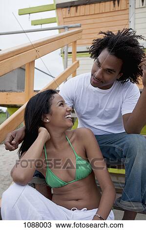 Stock Image - A young couple sitting on steps at the beach. Fotosearch