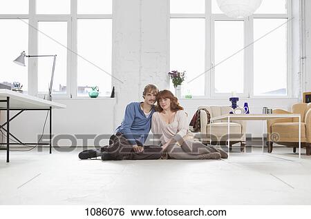 Stock Photograph - A young couple sitting side by side on the floor. Fotosearch