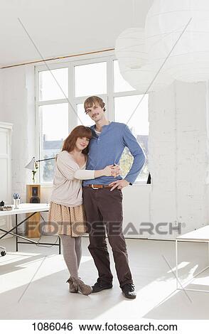 A young couple standing side by side arms around each other View Large Photo Image Stock Photograph - A young couple standing side by side arms around each other. Fotosearch