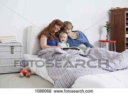 A young family in bed reading a picture book View Large Photo Image Stock Photo - A young family in bed reading a picture book. Fotosearch