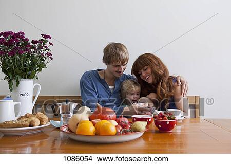 A young family sitting side by side having breakfast View Large Photo Image Picture - A young family sitting side by side having breakfast. Fotosearch