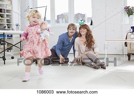 Stock Image - A young girl carrying a baby doll running around a living room. Fotosearch