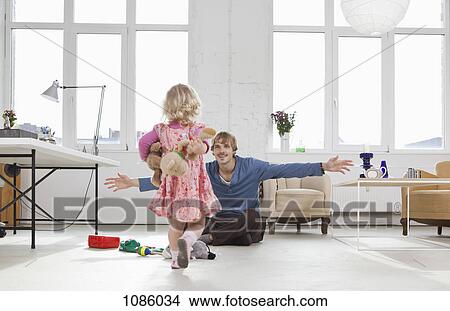 Picture - A young girl running towards her father sitting on the floor. Fotosearch