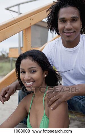 Stock Photo - A young happy couple sitting on steps at the beach. Fotosearch