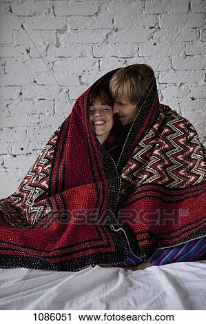Stock Image - A young happy couple wrapped in a blanket. Fotosearch