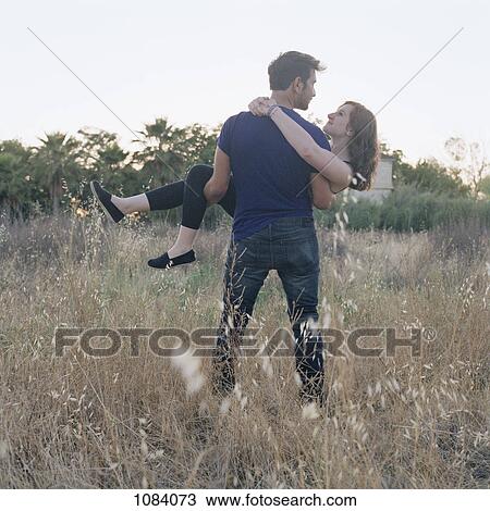 Stock Image - A young man carrying his girlfriend through a field. Fotosearch