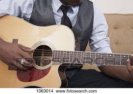Picture - A young man playing an acoustic guitar, focus on midsection. Fotosearch