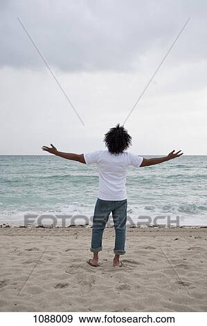A young man standing on beach with arms outstretched, rear view View Large Photo Image Stock Photo - A young man standing on beach with arms outstretched, rear view. Fotosearch