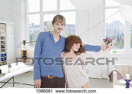 Stock Image - A young playful couple standing side by side holding hands. Fotosearch