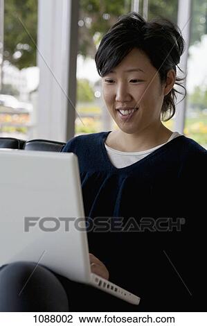 A young woman sitting on a sofa using a laptop View Large Photo Image Stock Image - A young woman sitting on a sofa using a laptop. Fotosearch