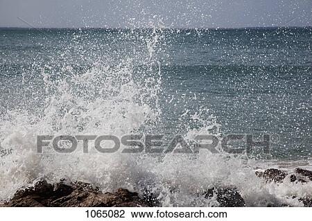 Stock Image - Detail of a wave splashing on rocks. Fotosearch