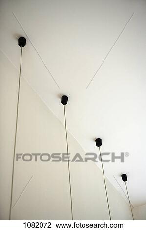 Stock Image - Four light fixtures with cables hanging down from ceiling. Fotosearch