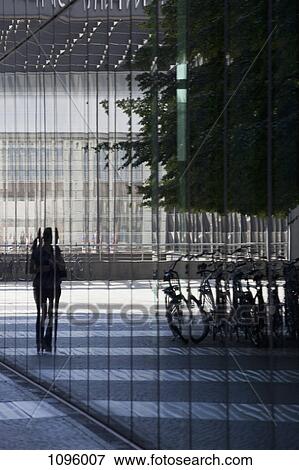 Stock Photo - Glass facade reflecting passer-by looking at parked bicycles. Fotosearch