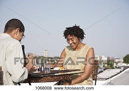 Over the shoulder view of a couple eating a meal on a rooftop terrace View Large Photo Image Stock Photo - Over the shoulder view of a couple eating a meal on a rooftop terrace. Fotosearch