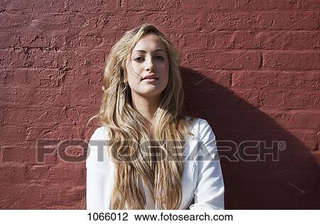 Stock Image - Portrait of a young woman leaning against a wall. Fotosearch
