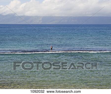 Stock Image - Senior man standing on surf board in ocean. Fotosearch