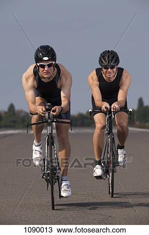 Stock Image - Two cyclists on racing bicycles cycling on a marked road. Fotosearch