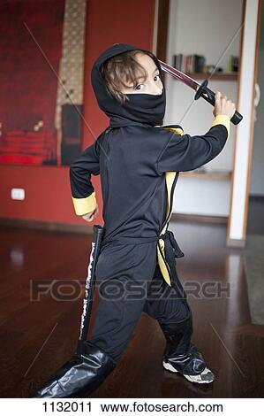 Stock Image - A boy dressed in a ninja costume swinging a samurai sword. Fotosearch