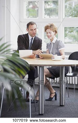 A businessman and businesswoman using a digital tablet in a meeting View Large Photo Image Stock Photo - A businessman and businesswoman using a digital tablet in a meeting. Fotosearch