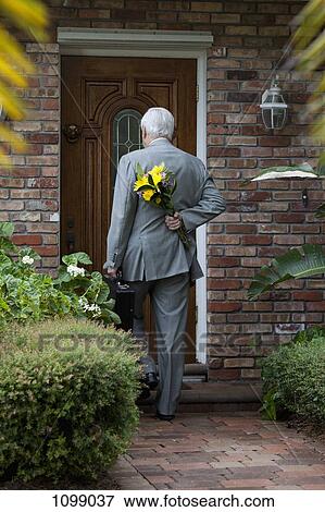Stock Photo - A businessman carrying flowers behind his back, arriving home. Fotosearch