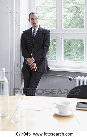 A businessman leaning against a window sill in a conference room View Large Photo Image Stock Photography - A businessman leaning against a window sill in a conference room. Fotosearch