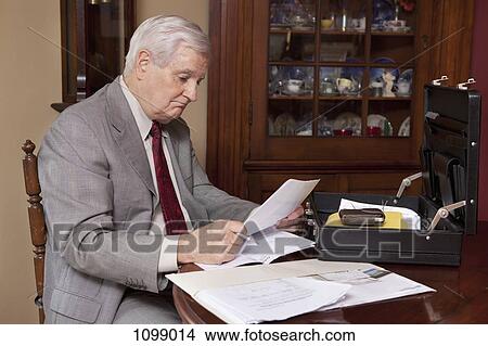 A businessman looking over paperwork at home View Large Photo Image Picture - A businessman looking over paperwork at home. Fotosearch