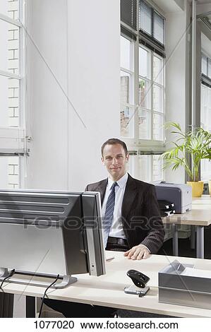 A businessman sitting at a desk in his office View Large Photo Image Stock Image - A businessman sitting at a desk in his office. Fotosearch