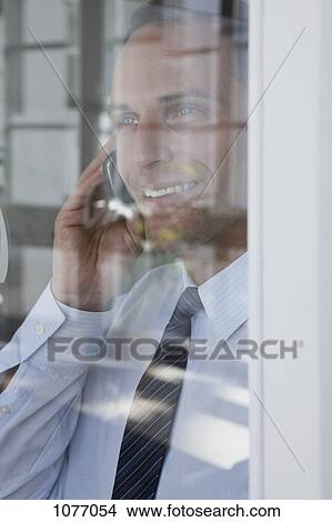 Picture - A businessman talking on a mobile phone, viewed through window. Fotosearch