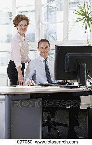 A businesswoman assisting a businessman sitting at a computer View Large Photo Image Stock Image - A businesswoman assisting a businessman sitting at a computer. Fotosearch