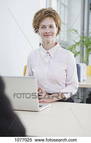A businesswoman with a laptop sitting at her office desk View Large Photo Image Stock Photography - A businesswoman with a laptop sitting at her office desk. Fotosearch