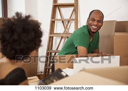 Stock Photo - A cheerful couple packing moving boxes, focus on man. Fotosearch