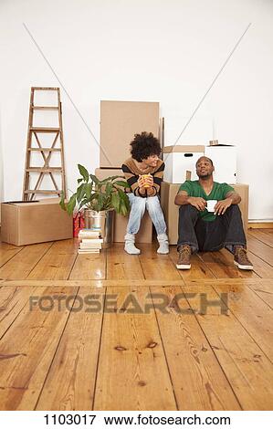 Stock Photo - A cheerful couple taking a coffee break while moving house. Fotosearch