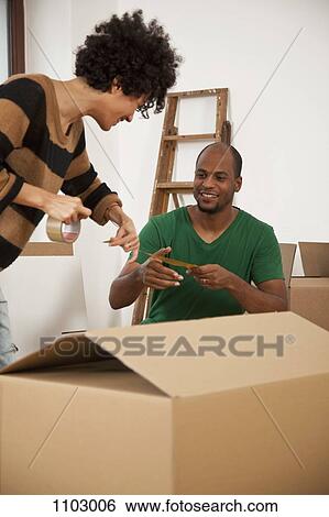 Stock Photograph - A cheerful couple working together to tape a moving box. Fotosearch