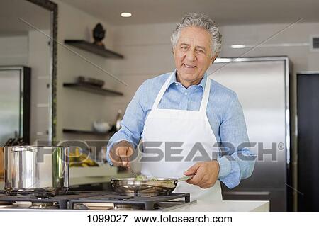 Stock Photo - A cheerful man cooking in a domestic kitchen. Fotosearch