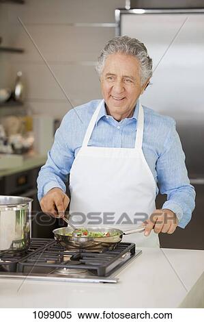 Stock Photography - A cheerful retired man cooking vegetables in a pan. Fotosearch