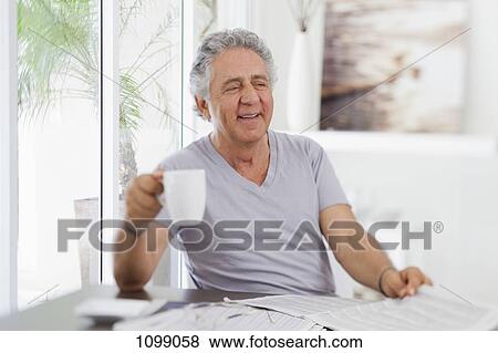 Stock Photo - A cheerful senior man holding a cup of coffee and a newspaper. Fotosearch