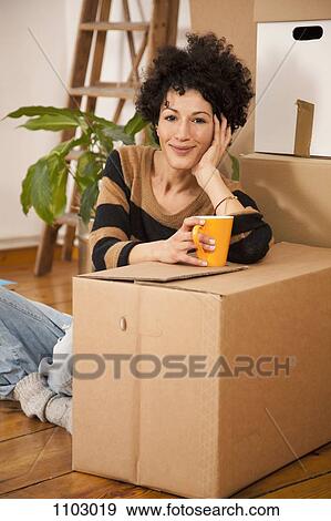 A cheerful woman taking a coffee break while moving house View Large Photo Image Stock Photo - A cheerful woman taking a coffee break while moving house. Fotosearch