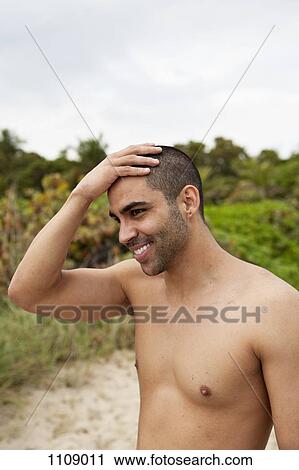 A cheerful young man rubbing his head at the beach View Large Photo Image Stock Image - A cheerful young man rubbing his head at the beach. Fotosearch