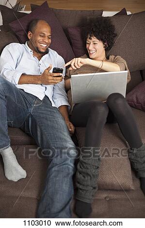 A couple reclining on a sofa sharing a laugh over something on a mobile phone View Large Photo Image Stock Image - A couple reclining on a sofa sharing a laugh over something on a mobile phone. Fotosearch