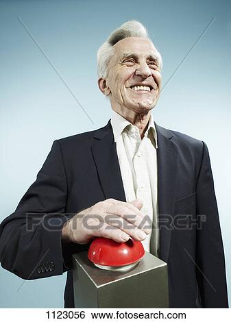 Stock Photograph - A grinning senior man pushing a red game show buzzer. Fotosearch