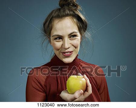 Stock Image - A hip young woman holding an apple and smiling. Fotosearch