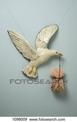 Stock Photo - A plastic bird carrying a sack in its beak, hanging on wall. Fotosearch