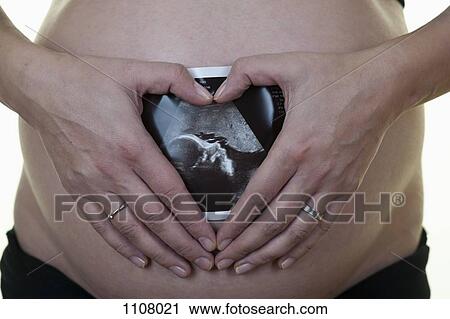 Stock Image - A pregnant woman holding an ultrasound printout against her belly. Fotosearch