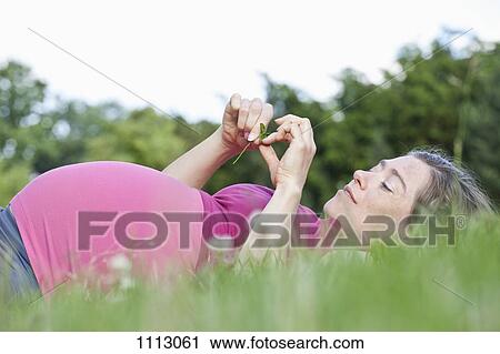 Stock Image - A pregnant woman lying in the grass, side view. Fotosearch