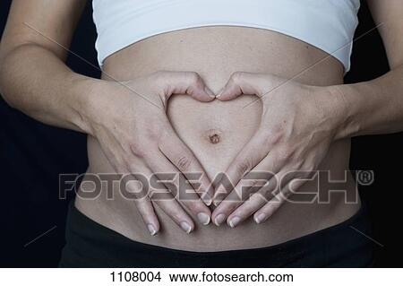 A pregnant woman making a heart shape with her hands on her abdomen View Large Photo Image Picture - A pregnant woman making a heart shape with her hands on her abdomen. Fotosearch
