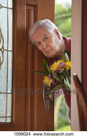 A senior man peeking through an open door with a bouquet of flowers View Large Photo Image Picture - A senior man peeking through an open door with a bouquet of flowers. Fotosearch
