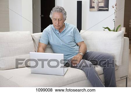 A senior man sitting on a couch using a laptop View Large Photo Image Stock Photo - A senior man sitting on a couch using a laptop. Fotosearch