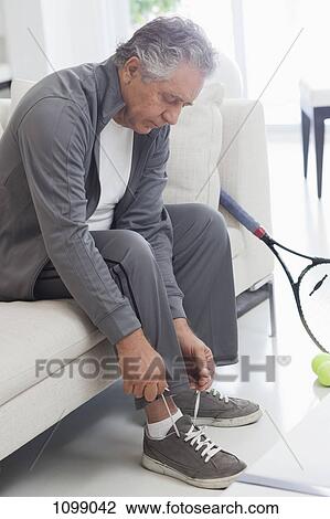 Stock Image - A senior man tying his shoelaces, preparing to play tennis. Fotosearch