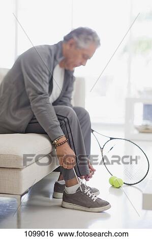 Stock Photograph - A senior man tying his shoelaces, preparing to play tennis. Fotosearch